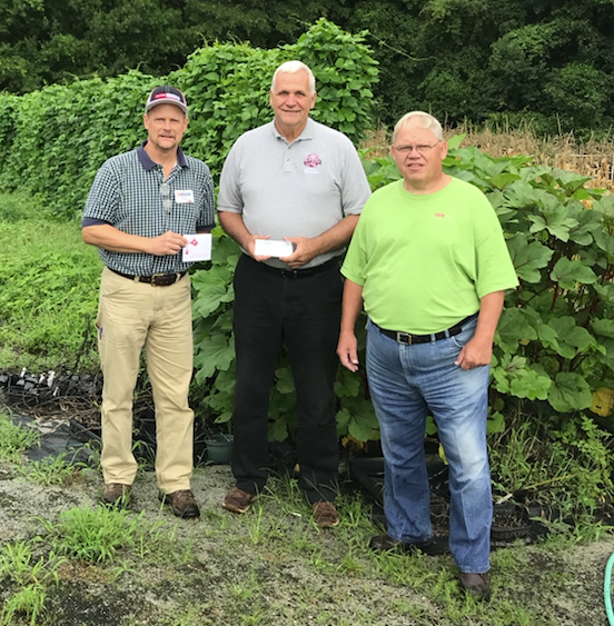 three men standing in a field holding a check