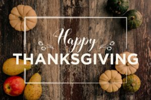 Happy Thanksgiving wrote in white letters with rustic wood background and small pumpkins in corners of picture
