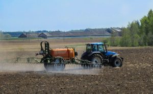 tractor spraying disked field with pesticides