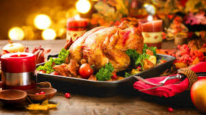 golden brown turkey on a black platter, garnished with greens, tomatoes, vegetables, holiday lights in the background
